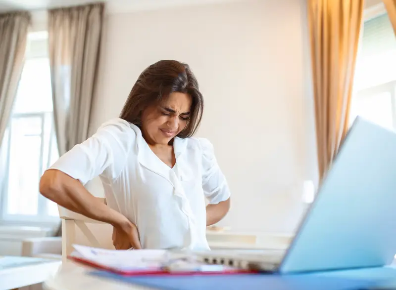 portrait-young-stressed-woman-sitting-home-office-desk-front-laptop-touching-aching-back-with-pained-expression-suffering-from-backache-after-working-laptop
